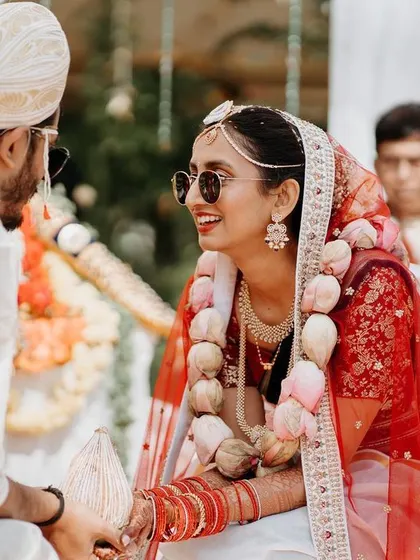 A cool bride, wearing sunglasses, shares a laugh with her groom during their sunny outdoor wedding ceremony.