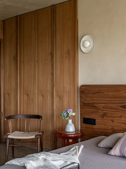 The bedroom is a serene retreat, with wood-paneled wardrobes and a simple, elegant chair. The design embraces the wabi-sabi philosophy of simplicity and intentional living.