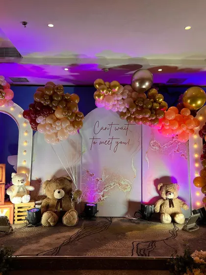 A stage setup for a baby shower with a "Can't wait to meet you!" backdrop, teddy bears, and dramatic lighting.