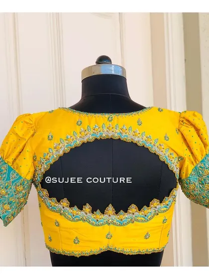 A playful and vibrant back design on a yellow blouse. The large keyhole cutout is framed with intricate embroidery that matches the work on the contrasting teal sleeve cuffs.