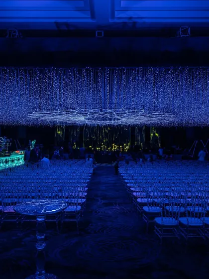 A view from the aisle shows the breathtaking scale of the starlit ceiling installation. The combination of the light canopy and ghost chairs creates a modern, ethereal look for the guest seating area.