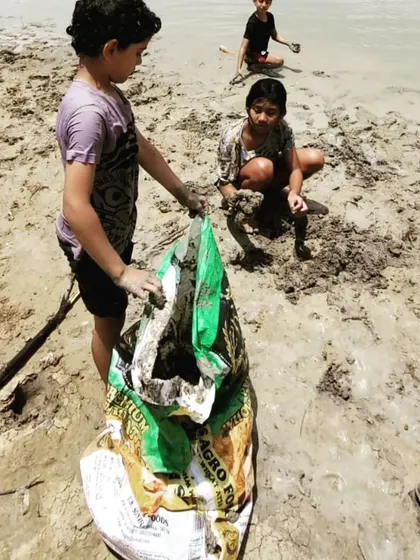 Teamwork makes the work lighter. Children work together to fill a sack with clay, a lesson in collaboration and shared effort.