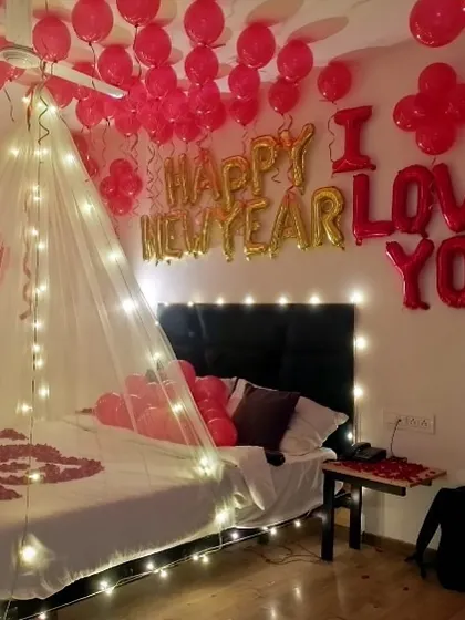 A festive room decoration for a New Year and romantic celebration, featuring "Happy New Year" and "I Love You" foil balloons, a light canopy, and red balloons.