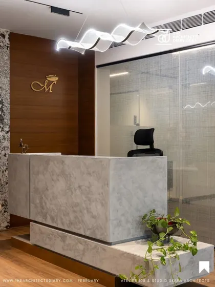 The reception desk from the Meghana Foods office feature, showcasing the blend of concrete-finish surfaces, wood paneling, and a dramatic light fixture.