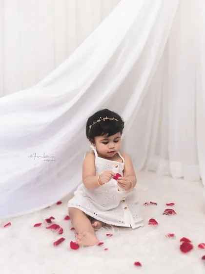 A simple and pure portrait of a baby girl with red rose petals. The clean white background and pop of color create a striking and artistic image.
