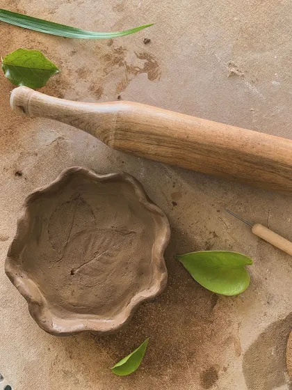 A hand-built bowl with a leaf impression, next to the rolling pin used to make it. A beautiful connection to nature.