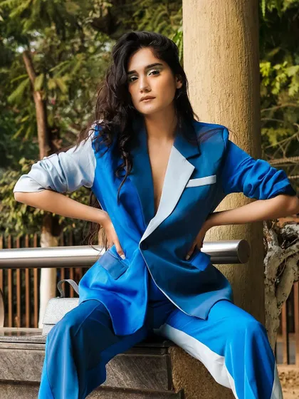 A striking two-tone blue power suit, shot outdoors. The model's strong pose and direct gaze make this a commanding image for a corporate fashion brand.