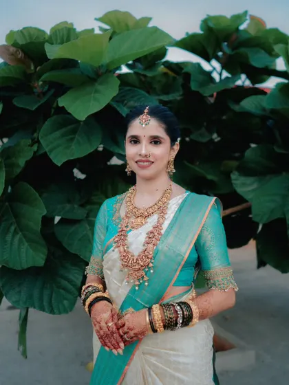 A lovely portrait of the bride against a backdrop of lush green leaves, her traditional attire looking vibrant and beautiful in the natural light.