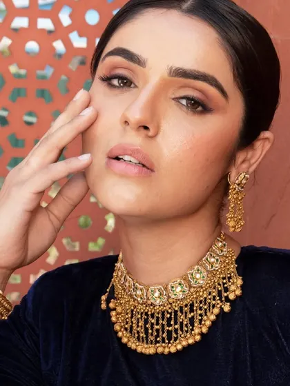 A close-up beauty shot from a jewellery campaign. The model is wearing a traditional gold choker with intricate details, styled with a deep blue velvet top for a rich, royal look suitable for any wedding celebration.
