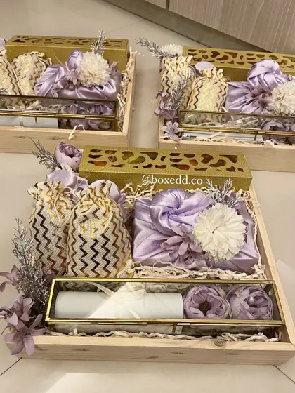 A stunning wedding invitation hamper designed with a lavender and gold theme. These wooden trays include a scroll invitation in a glass box, furoshiki-wrapped gifts, and sweet pouches, creating a truly luxurious experience for your guests.