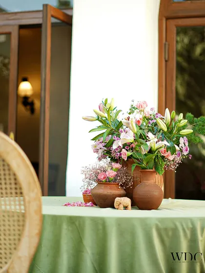 Another beautiful centerpiece, featuring terracotta pots of different sizes filled with fresh lilies and other pastel flowers, set against a sage green tablecloth.