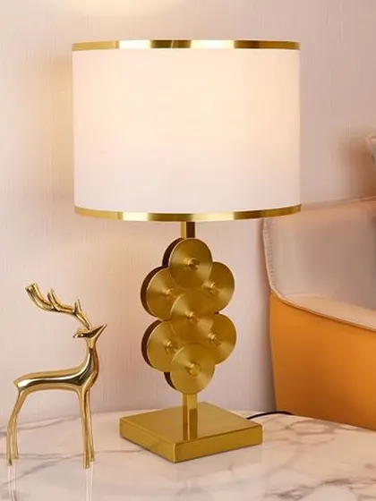 This elegant lamp features a unique base made of stacked golden discs on a square pedestal. Paired with a white and gold-trimmed drum shade, it adds a touch of modern luxury and brightens up any space.
