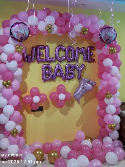 A close-up of the pink and white balloon arch with "WELCOME BABY" foil letters and an "It's a Girl" foot-shaped foil balloon.
