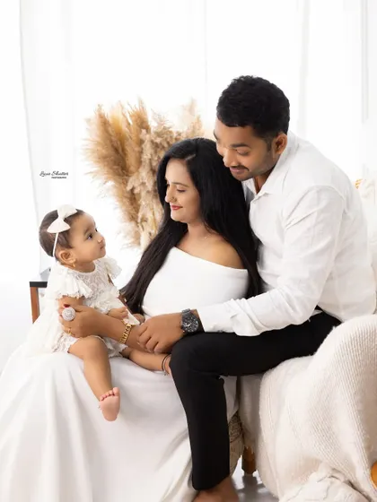 A tender family moment, with the parents and their baby sharing a quiet, loving gaze. The coordinated white outfits create a clean and classic look.