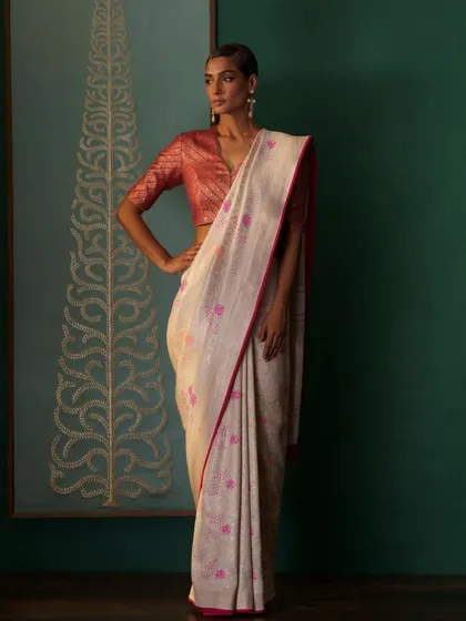 A soft, handwoven saree with delicate pink motifs, paired with a contrasting red brocade blouse. This look shows how to play with color and texture for a sophisticated yet understated effect.