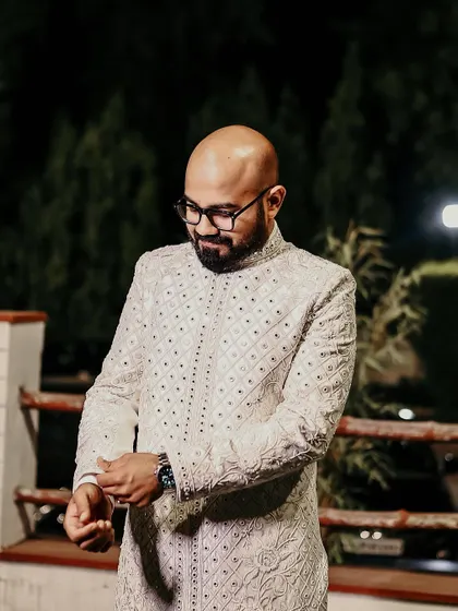 A dapper portrait of the groom, adjusting his cuffs and looking sharp in his elegant white sherwani.