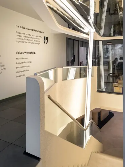 A bar of light pierces through the two levels, vertically anchoring the space. The reflective ceiling above captures abstract movements from below, adding a dynamic and playful element.