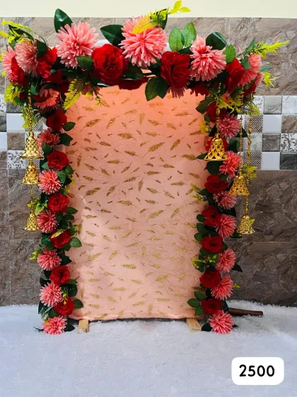 Pink and red artificial flowers surround a pink patterned panel with hanging bells in our ₹2,500 ready-made Ganpati design.