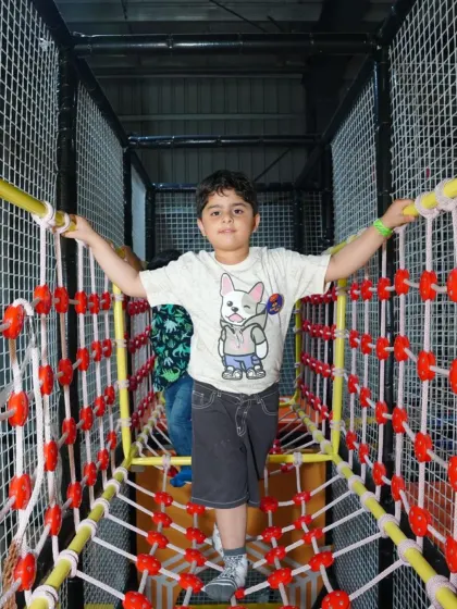 A young adventurer carefully makes his way across a netted rope bridge, one of the many challenges in our soft play jungle gym.
