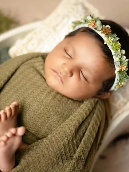A newborn wrapped in an olive green waffle wrap with a succulent headband, showcasing a beautiful, earthy theme.