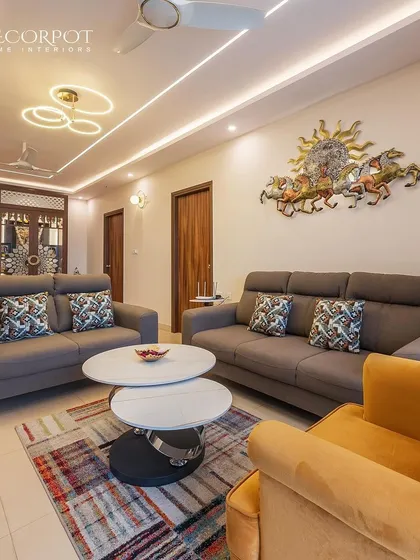 A cozy living room with a comfortable grey sofa, a colorful rug, and a bright yellow armchair that adds a pop of color. The horse-themed wall art and modern false ceiling complete the look.
