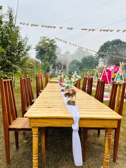 A long wooden dining table set up outdoors with simple, elegant floral centerpieces, ready for a family-style meal.