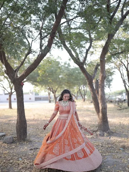 A wide shot showing the bride in her beautiful orange lehenga, twirling in a natural setting. The look is perfect for an outdoor engagement ceremony.