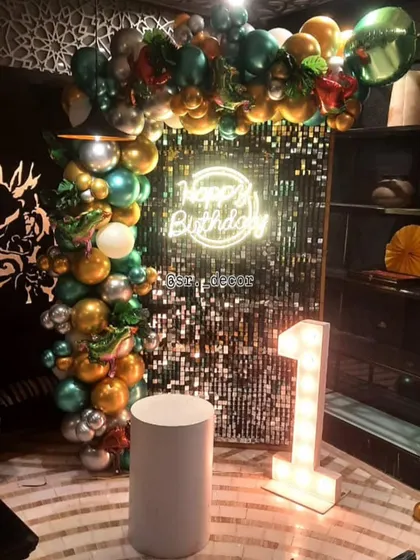 A fun jungle theme for a first birthday, featuring a green and gold balloon arch against a shimmer wall, complete with animal-themed details.
