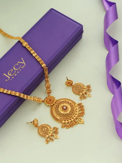 A beautiful composition of a gold necklace set with its purple gift box and a ribbon. This styling makes the product look like a perfect, ready to give present for a special occasion.