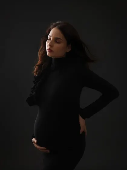 A contemplative and moody portrait. The dark background and simple black dress create a dramatic and intimate image that focuses on the mom-to-be's inner world.