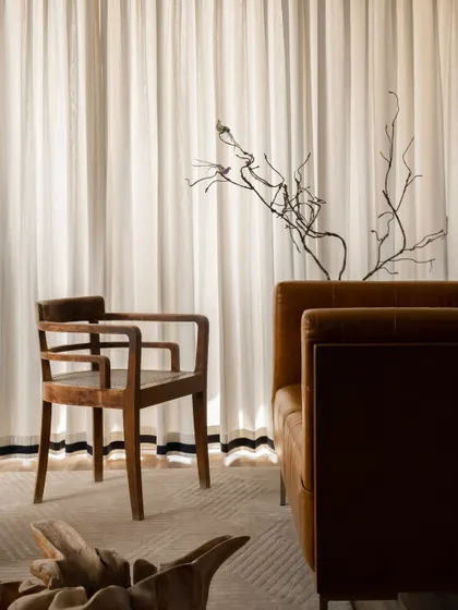 The story of a space is often told in its details. Here, a handcrafted wooden chair with a cane seat brings a sense of tradition, creating a beautiful dialogue with the rich texture of a camel-toned leather sofa. It is a pairing rooted in contrast yet tied together by an earthy, timeless tone.