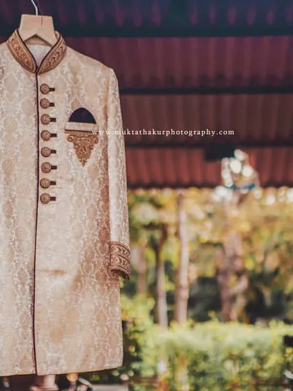 A detailed shot of the groom's wedding sherwani, focusing on the intricate buttons and embroidered pocket square.