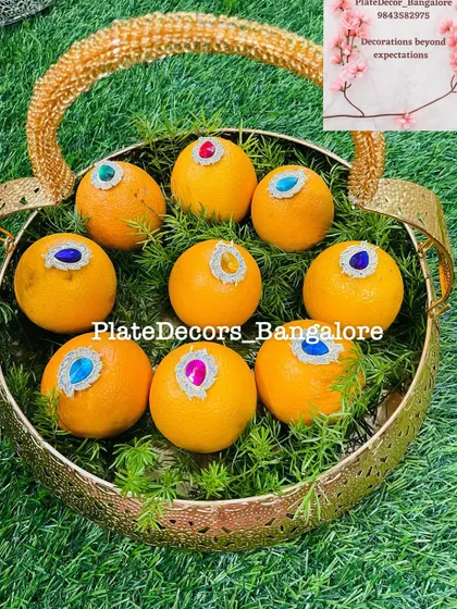 A golden basket filled with oranges, each adorned with a large, colorful kundan stone. A simple yet beautiful way to present fruits.