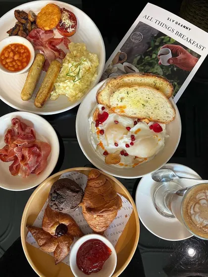 A full English breakfast spread alongside Cilbir (Turkish eggs) and a basket of fresh croissants. Breakfast for queens.