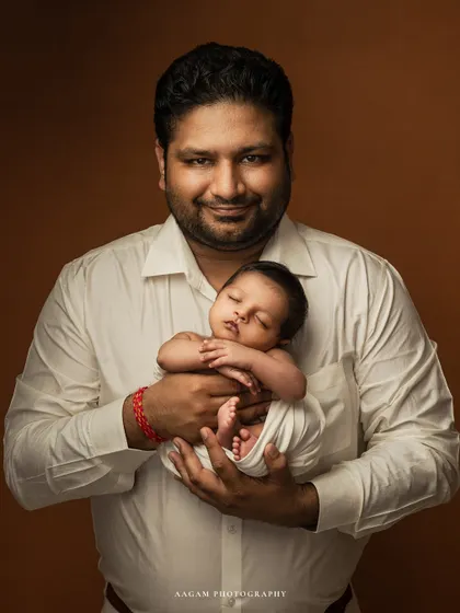 A proud father holds his sleeping newborn close to his heart. A classic fine art portrait that captures the profound bond between a dad and his new baby.