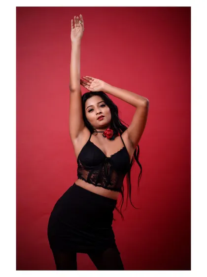 A full-length shot of a model in a black dress against a red background. The pose is strong and the color contrast is striking.