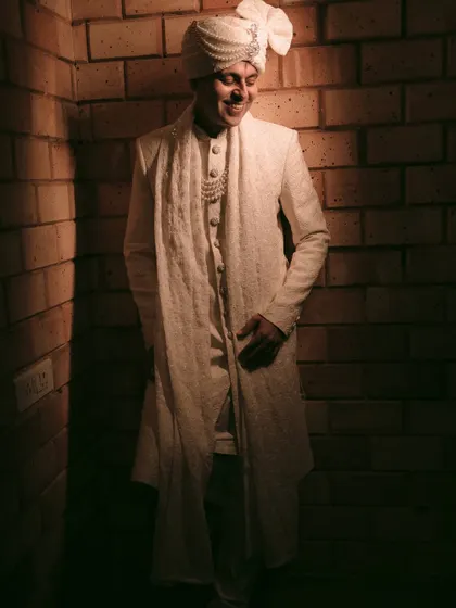 A stylish portrait of the groom in his elegant white sherwani, captured with dramatic lighting.