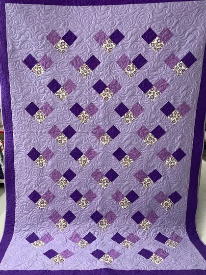 A simple and lovely quilt with a pattern of cascading purple hearts or squares, set against a lavender background with swirling quilting.