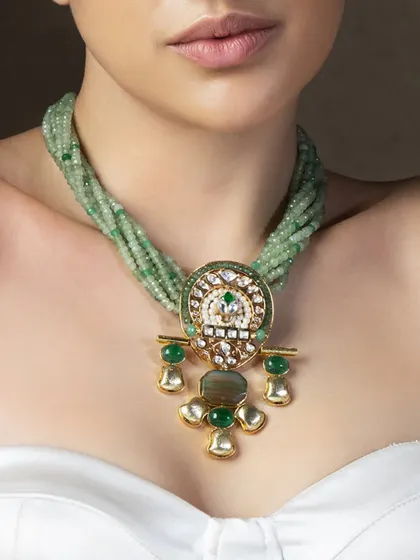 This unique necklace features strands of light green beads with a central pendant inspired by traditional Indian motifs, perfect for a destination wedding.