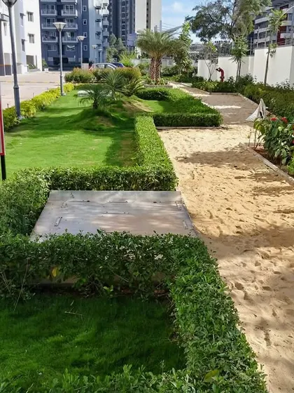 A landscaped area within a modern residential complex, featuring a sandpit for recreation alongside formal hedges and lawn patches. This shows my work in creating functional amenities for residents.