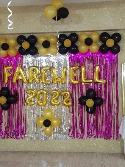 A simple yet effective setup for a corporate farewell party. This backdrop features a tinsel curtain, 'Farewell 2022' foil balloons, and flower-shaped balloon accents in black and gold.