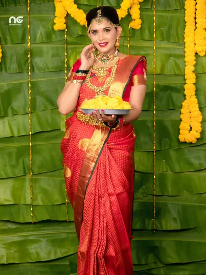 A full-length shot of the model, looking radiant in her red saree and gold jewellery.