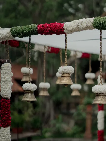 Traditional brass bells adorned with flowers, hanging from the mandap structure.
