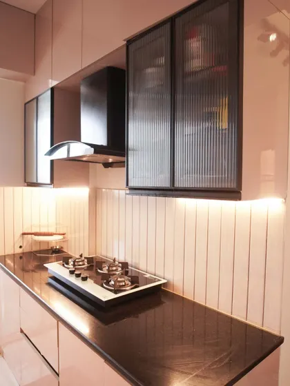 A charming parallel kitchen with soft pink glossy cabinets and a black granite countertop. The design is complemented by a vertically tiled backsplash and under-cabinet lighting, creating a warm and inviting space.