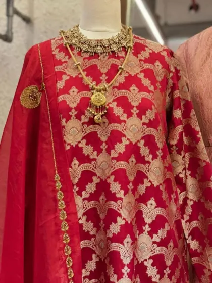 A close-up of the red Banarasi suit, showcasing the intricate gold weaving and the stunning layered necklace that completes this regal ensemble.