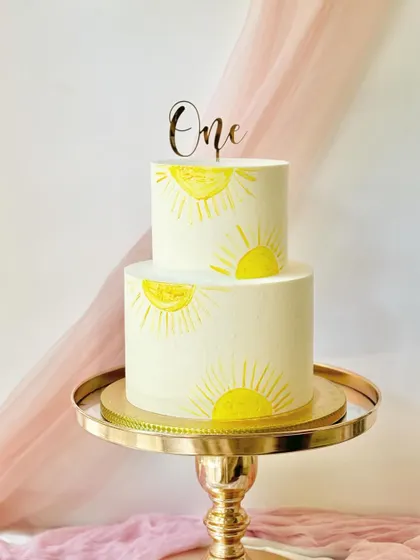A "You Are My Sunshine" themed first birthday cake. This simple and sweet two-tiered cake is hand-painted with cheerful suns.