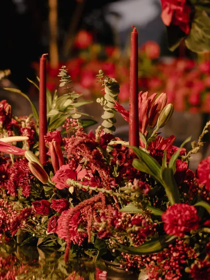 A macro shot of a centerpiece, focusing on the textures and deep red tones of the flowers. The careful layering of different blooms creates a rich, velvety effect.