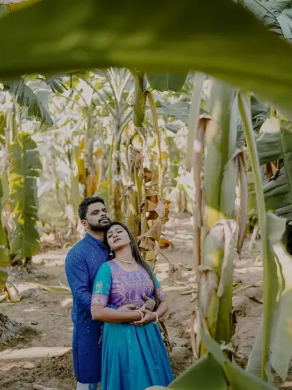 A creative pre-wedding shot of a couple surrounded by the large green leaves of a banana plantation, creating a lush and unique backdrop.