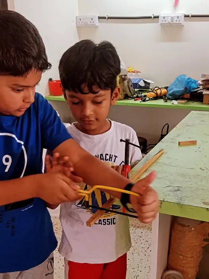 A helping hand costs nothing. Here, an older student helps a younger one with his project, showcasing the collaborative spirit of our workshops.