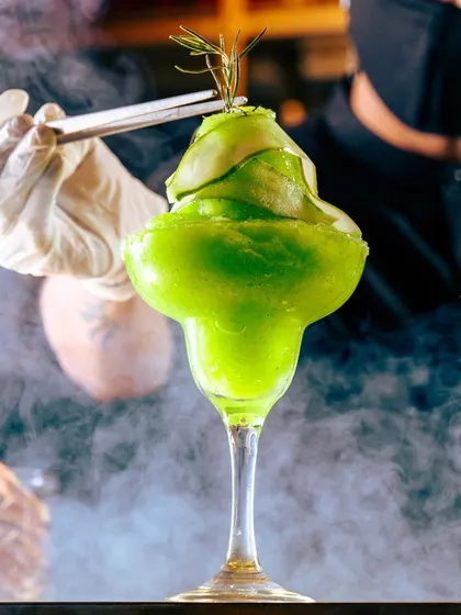 The ambiance and overall experience are essential. This dramatic green cocktail, garnished with cucumber ribbons, is designed to stand out.